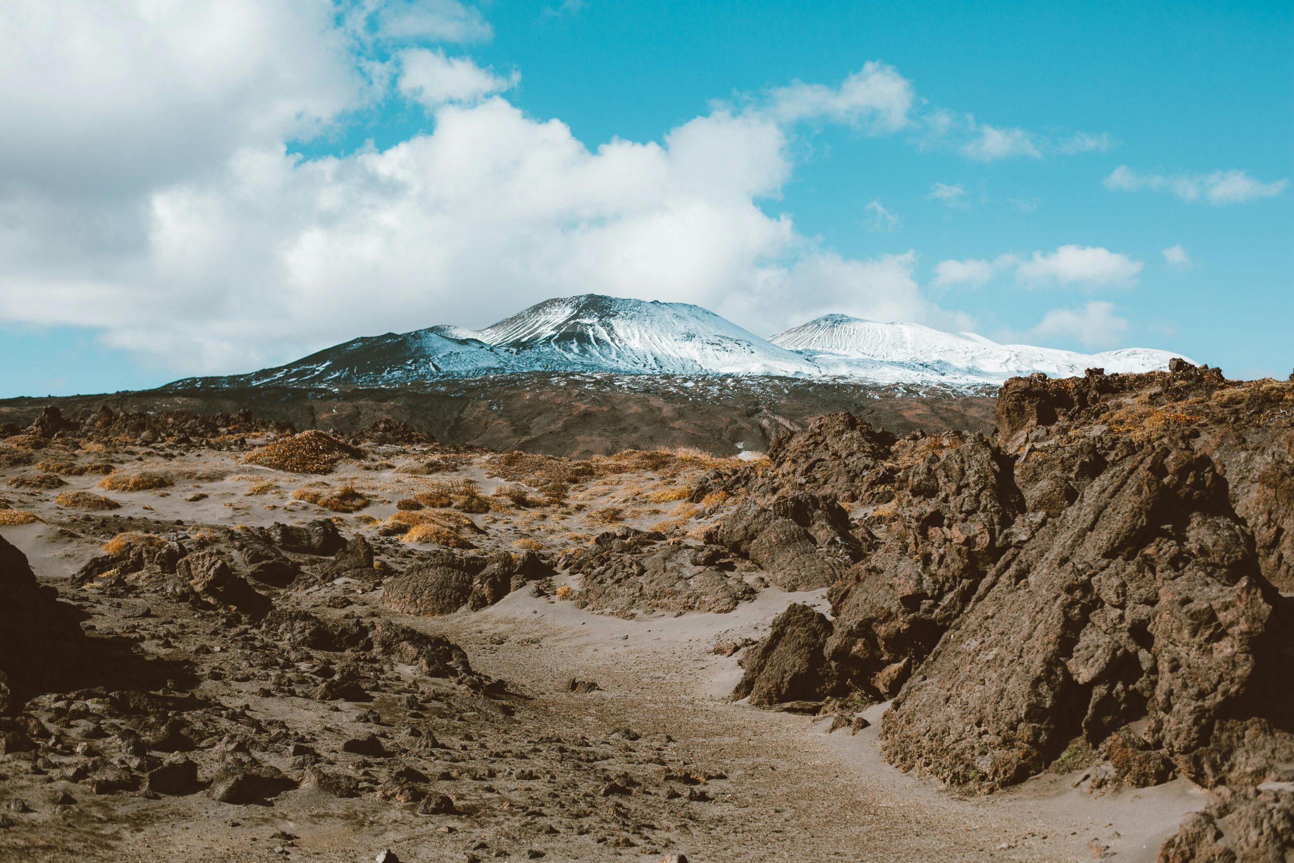Picturesque view of distant mountains with snow on slopes surrounded by rocky terrain under cloud sky